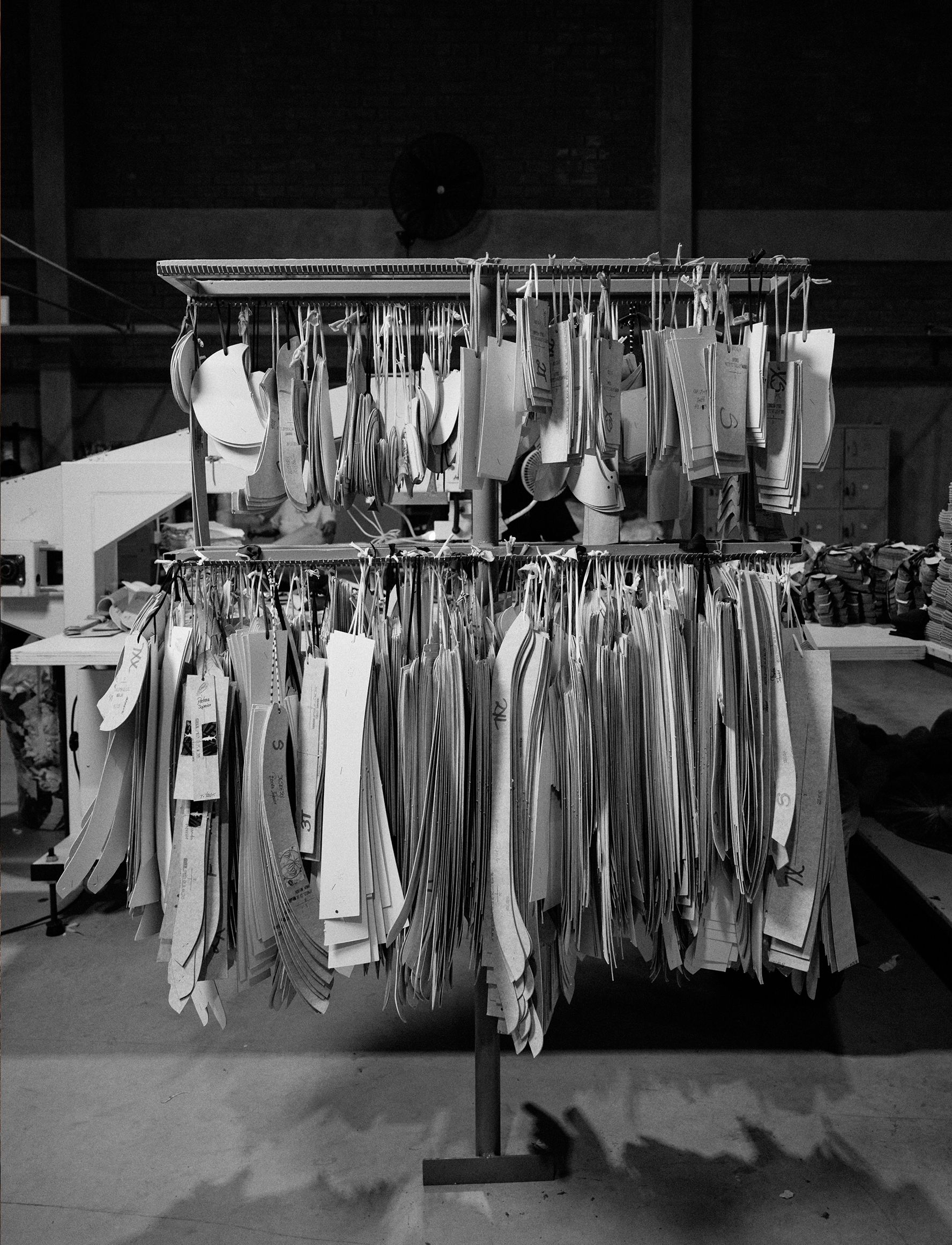 A black-and-white photo of racks filled with hanging garment pattern templates in various sizes inside a manufacturing facility.