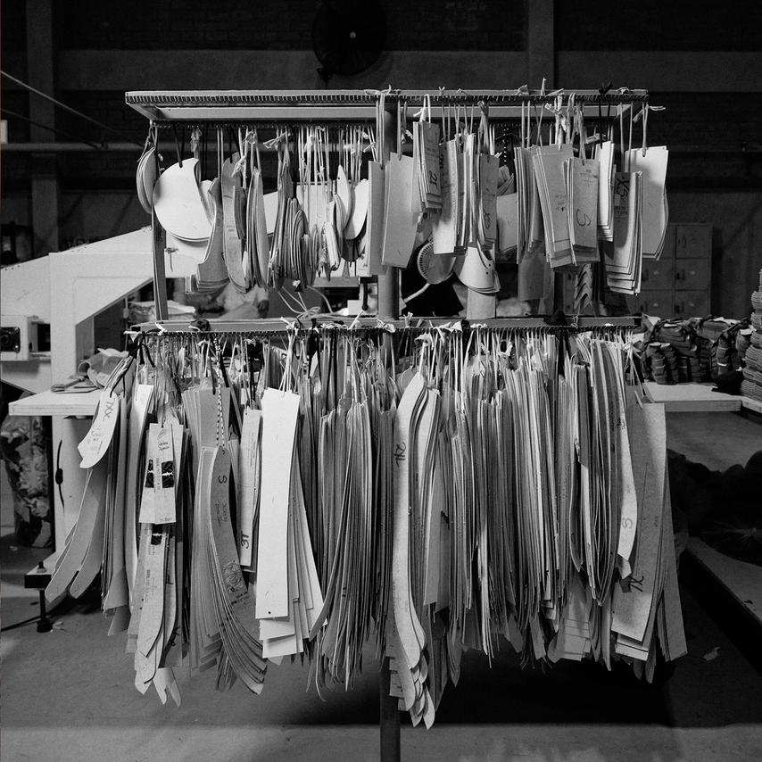 A black-and-white photo of racks filled with hanging garment pattern templates in various sizes inside a manufacturing facility.