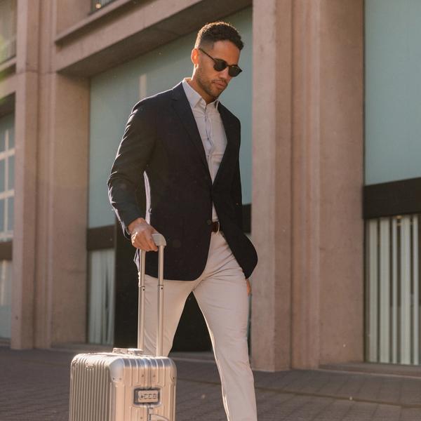 Man outside wearing a blue blazer while pushing a rolling suitcase