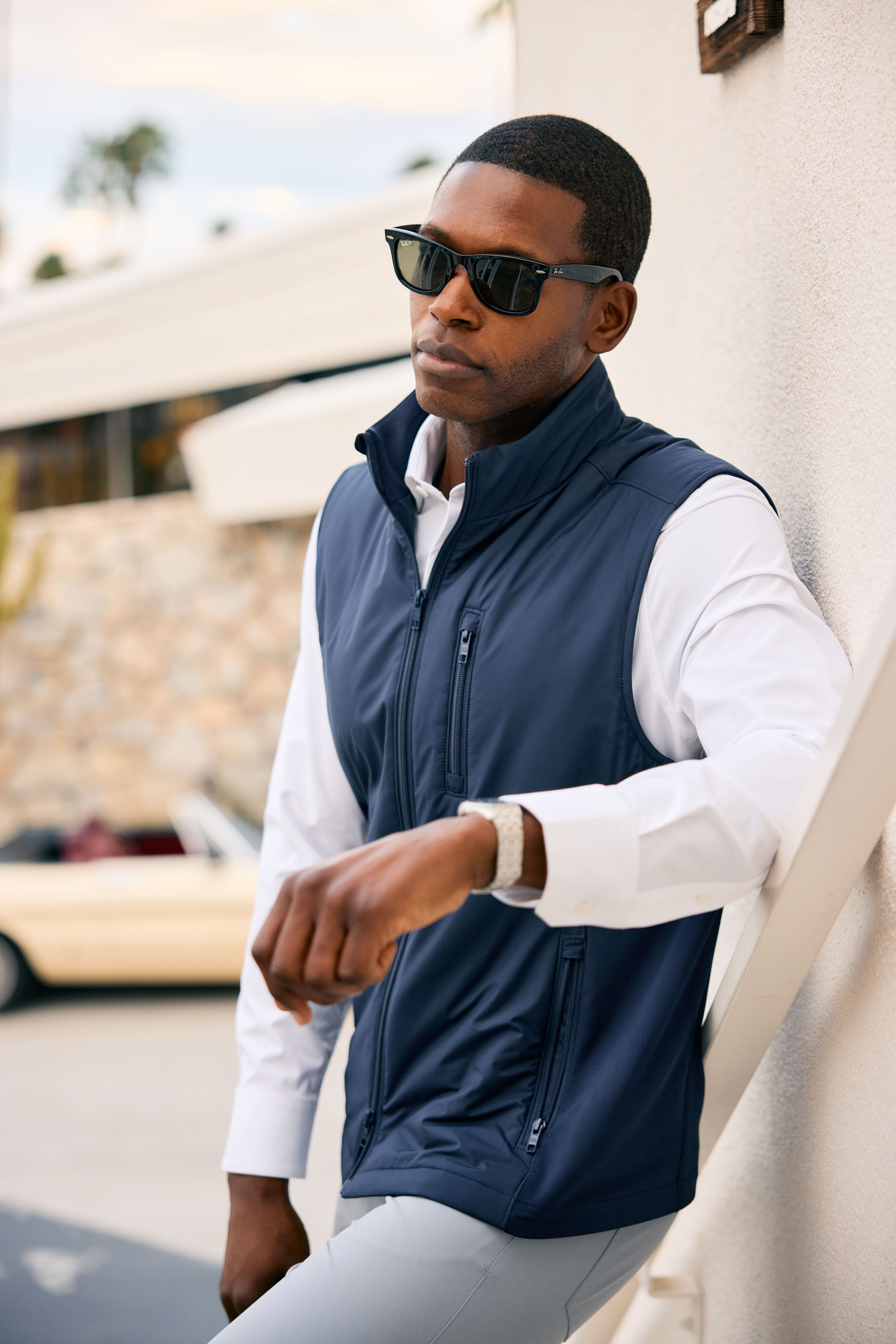 Man in sunglasses wearing a navy vest over a white dress shirt with gray pants