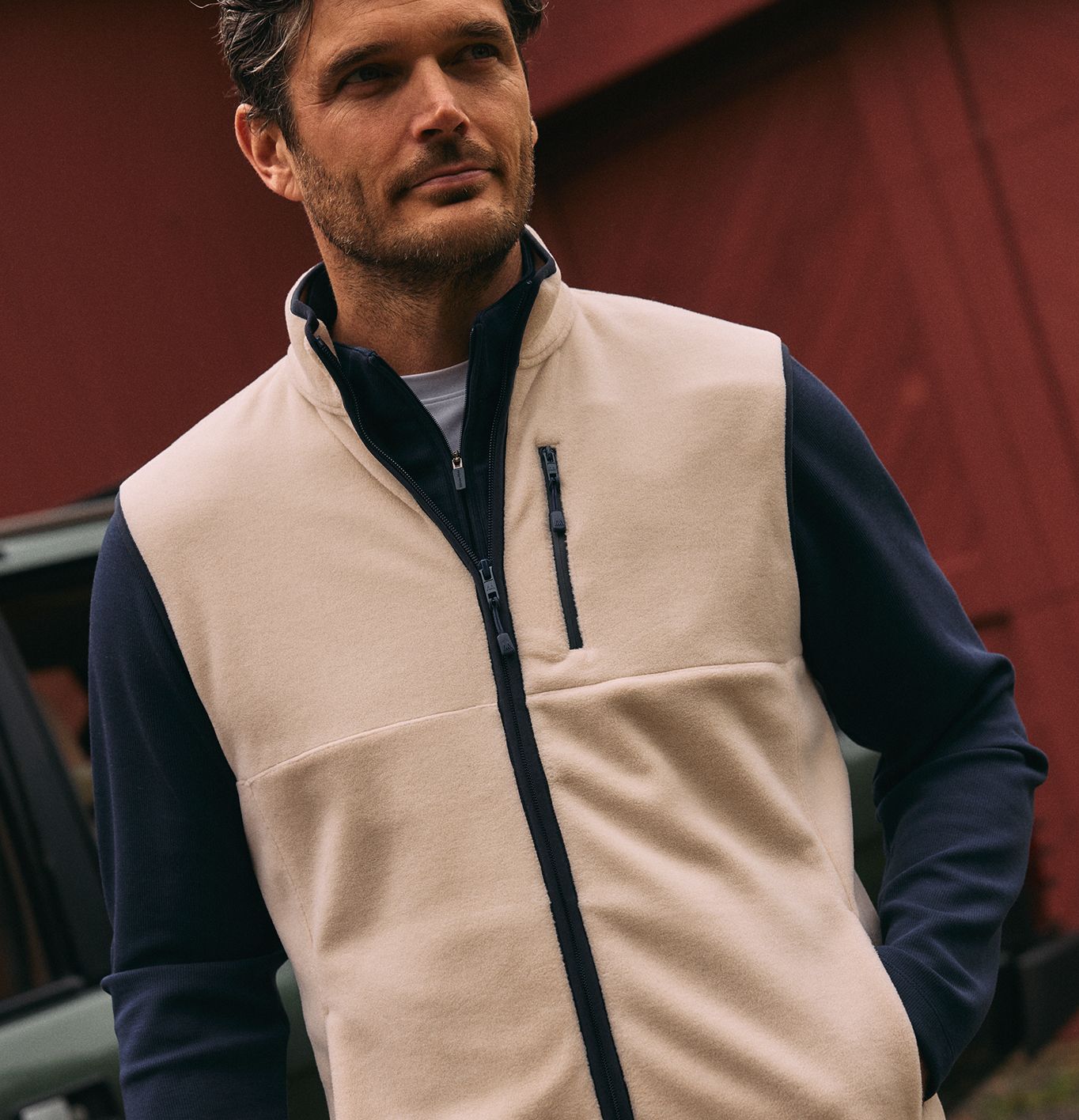A man wearing a beige fleece vest with a dark blue collar and zipper trim over a dark long-sleeve shirt.