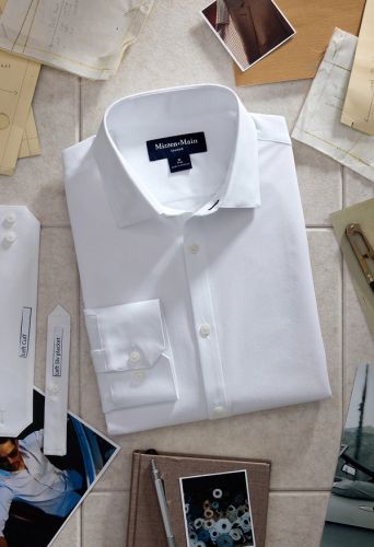 Folded white Mizzen+Main dress shirt laid flat among sewing pattern pieces, photographs and a notebook