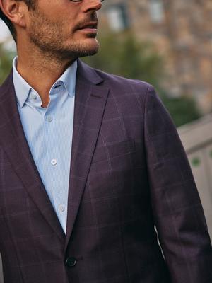 A close-up shot of a man wearing eyeglasses, a light blue micro-grid dress shirt, and a dark plum windowpane blazer.