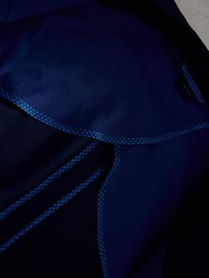 A close-up interior shot of a dark navy jacket showing the smooth inner lining, patterned seam binding trim, and a brand tag.