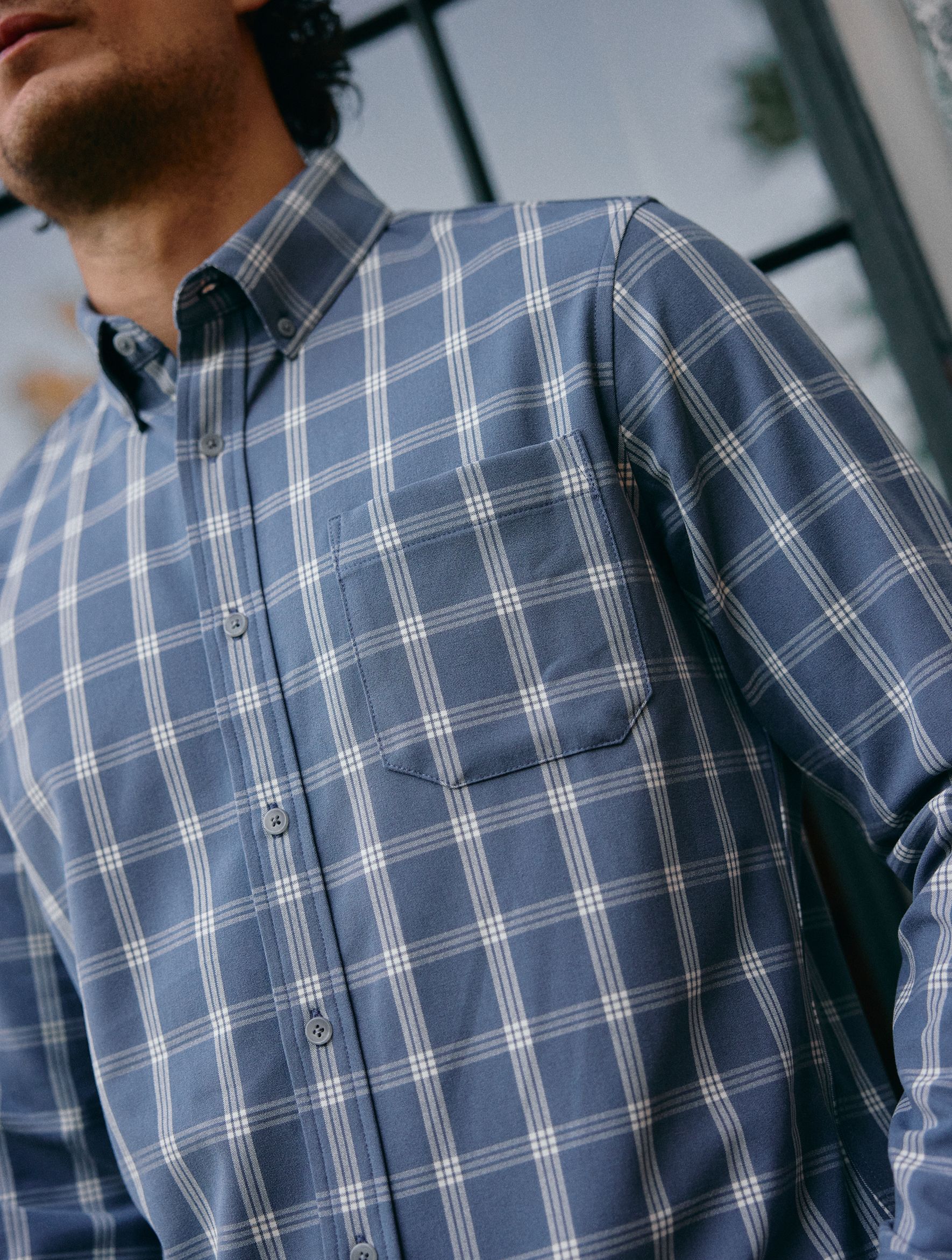 A close-up shot of a man wearing a blue and white plaid button-down shirt with a chest pocket.