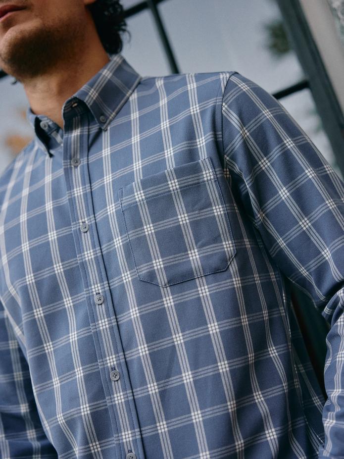 A close-up shot of a man wearing a blue and white plaid button-down shirt with a chest pocket.