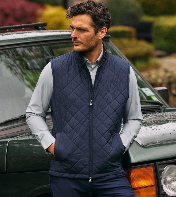 Man in a navy quilted Brentwood Vest over a light gray shirt, leaning against a vintage green car.