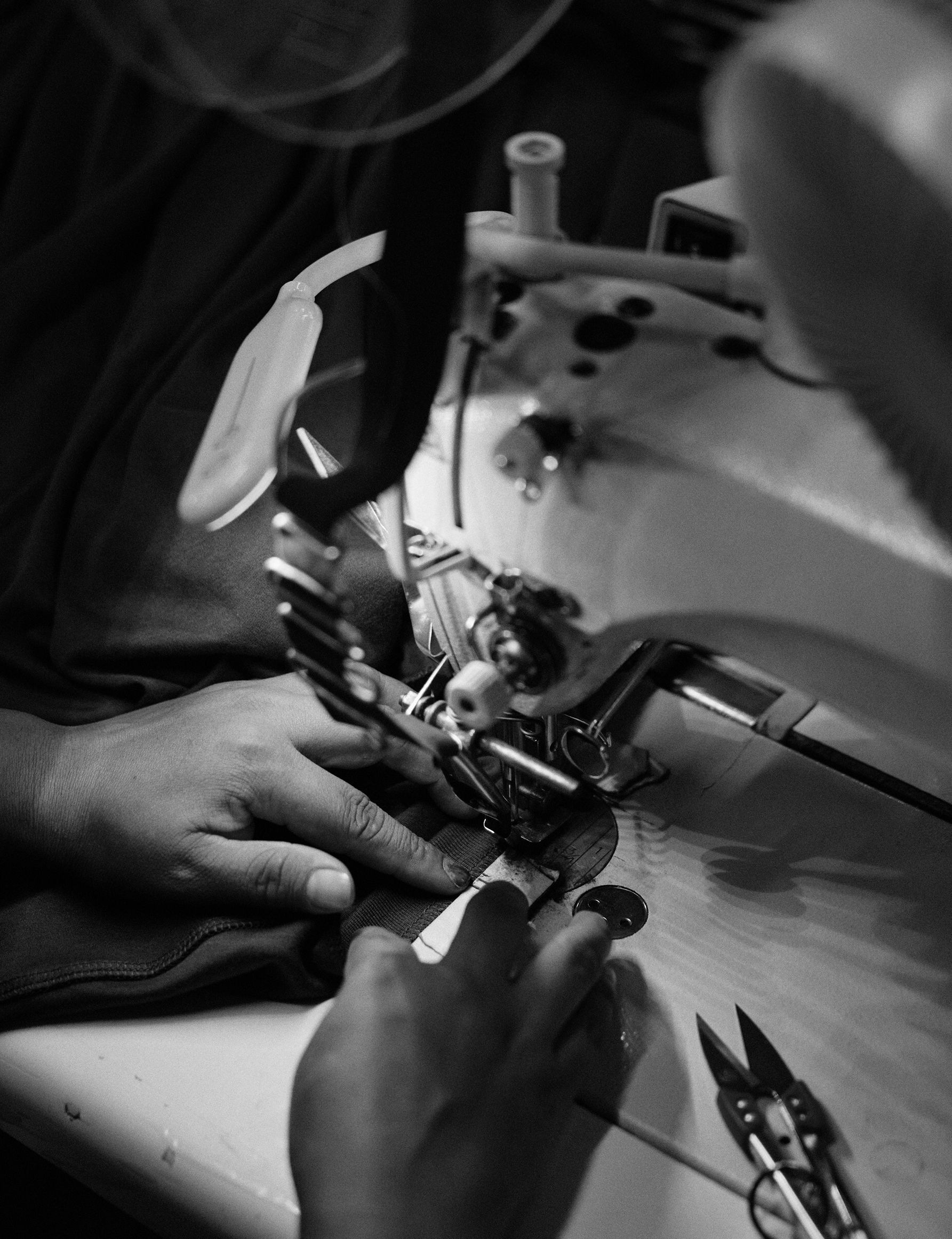 Black-and-white shot of a seamstress guiding fabric under the needle of an industrial sewing machine.