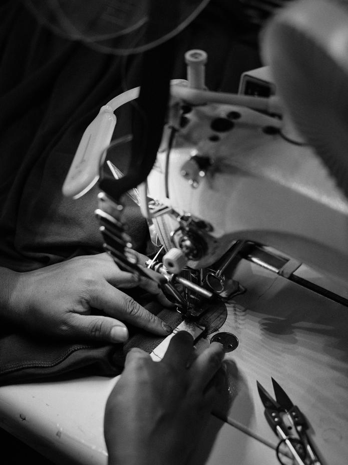 Black-and-white shot of a seamstress guiding fabric under the needle of an industrial sewing machine.