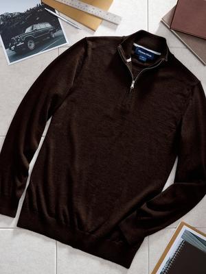 A top-down product flat-lay photo of a dark brown quarter-zip sweater set among office and design props on a tiled surface.