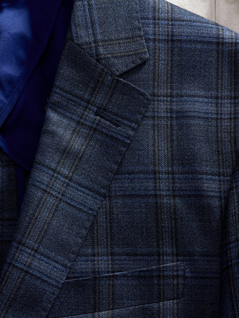 Macro close-up shot focusing on the lapel and textured weave of a dark blue plaid suit jacket.