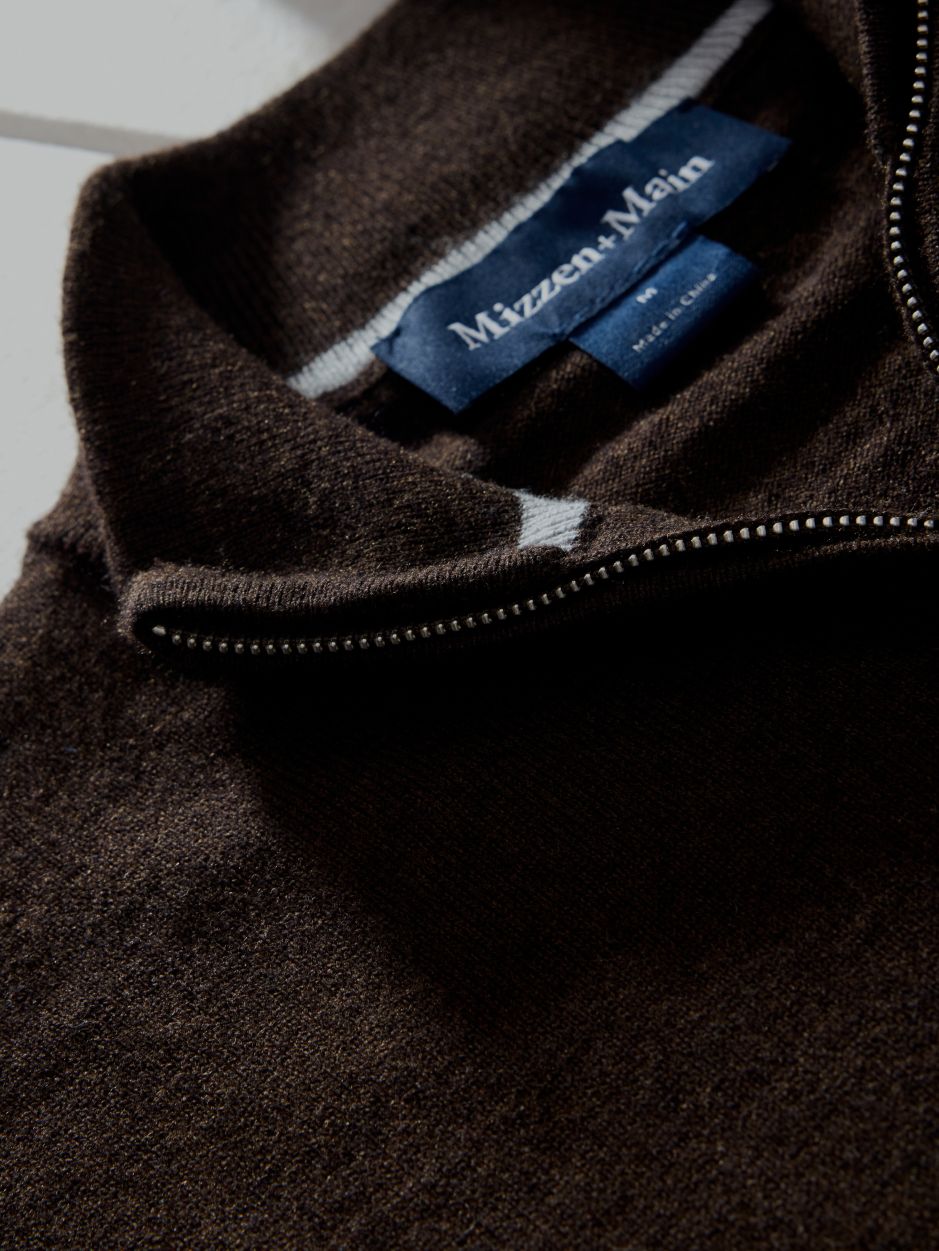 A macro detail shot focusing on the inner collar, woven brand label, and metal zipper track of a dark brown quarter-zip sweater.