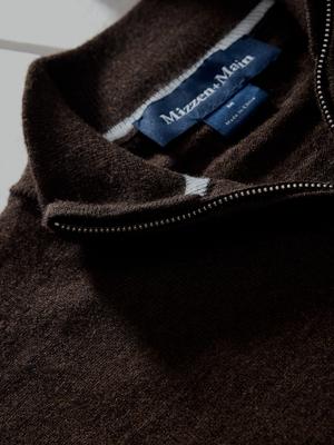 A macro detail shot focusing on the inner collar, woven brand label, and metal zipper track of a dark brown quarter-zip sweater.