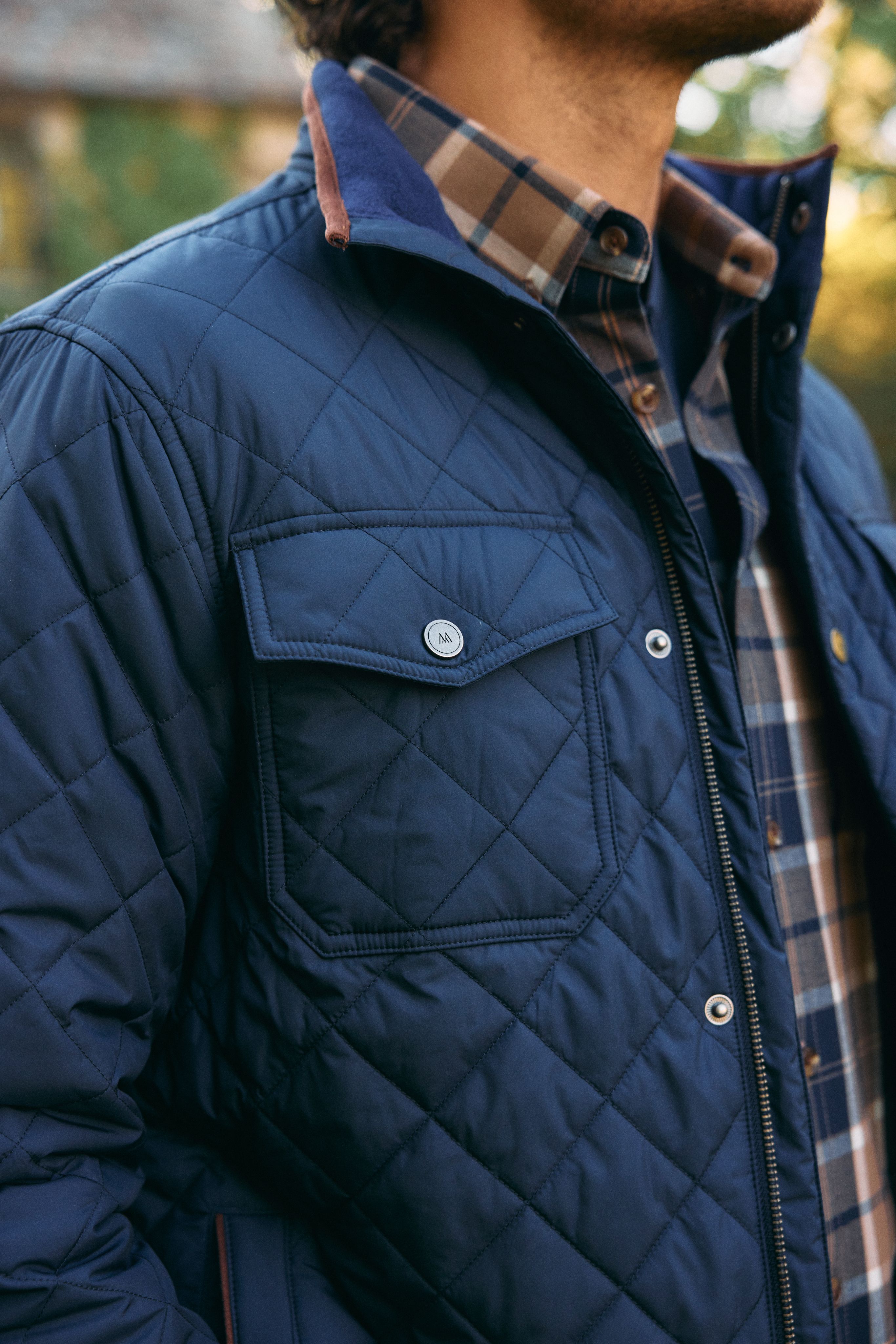 Close-up of a navy quilted shirt jacket layered over a plaid flannel shirt