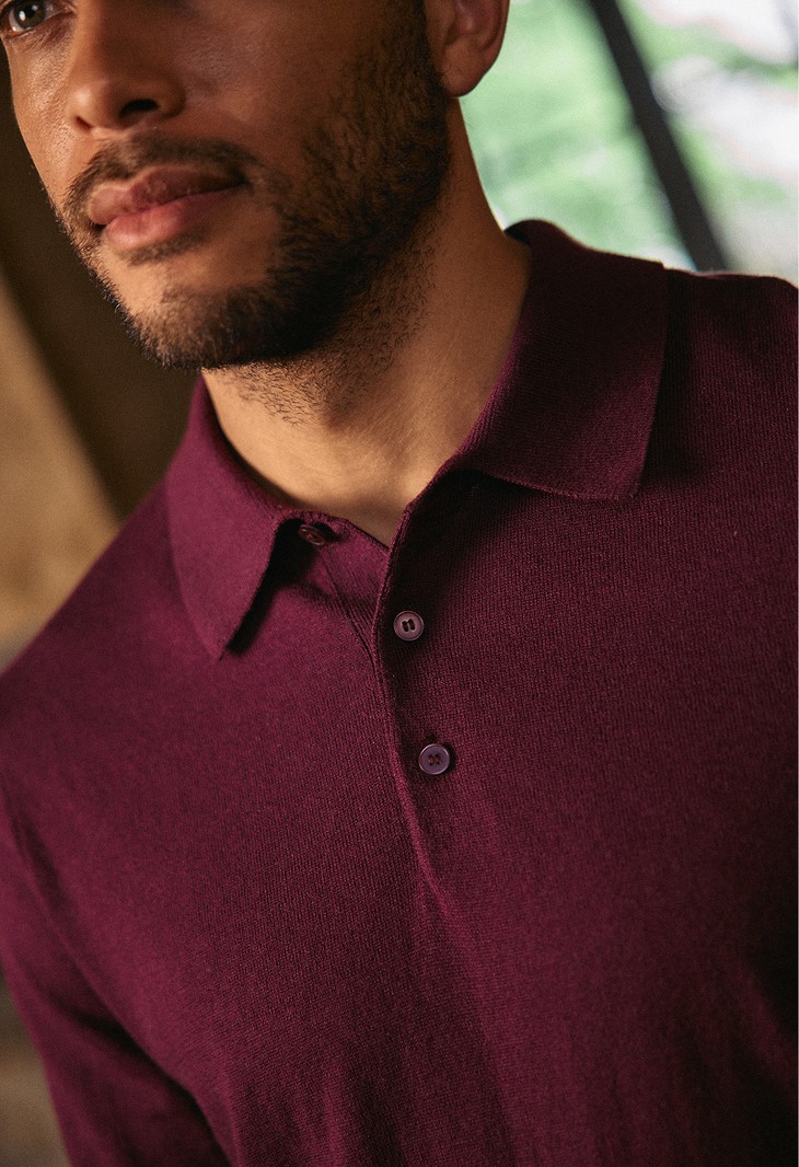 Close-up of a man wearing a burgundy knit polo sweater with a buttoned placket.