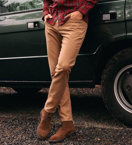 A close-up shot focusing on tan pants and brown suede boots worn by a man leaning against a green SUV.