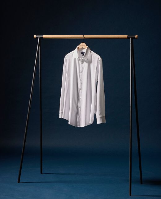 The Leeward dress shirt in white on a wooden hanger against a deep blue backdrop.