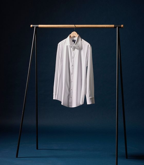 The Leeward dress shirt in white on a wooden hanger against a deep blue backdrop.