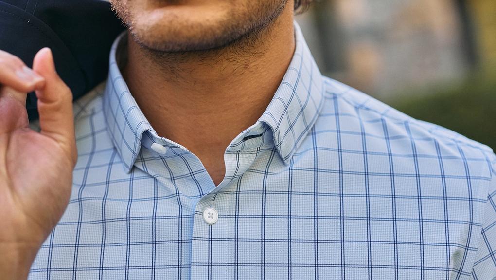 Close-up of a man in a light blue windowpane check dress shirt holding a navy jacket over his shoulder