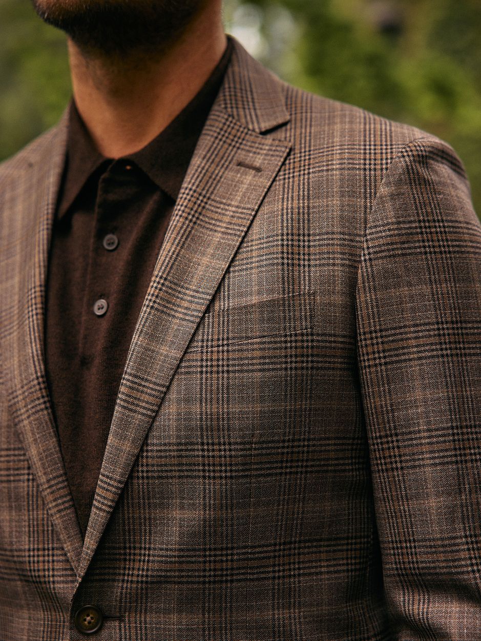 A close-up shot of a man wearing a brown plaid blazer over a dark brown knit polo shirt.