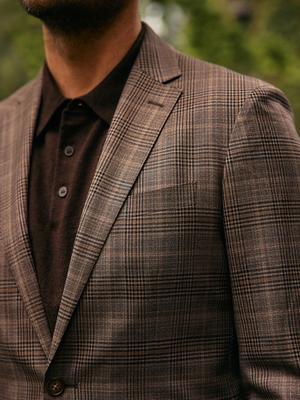 A close-up shot of a man wearing a brown plaid blazer over a dark brown knit polo shirt.