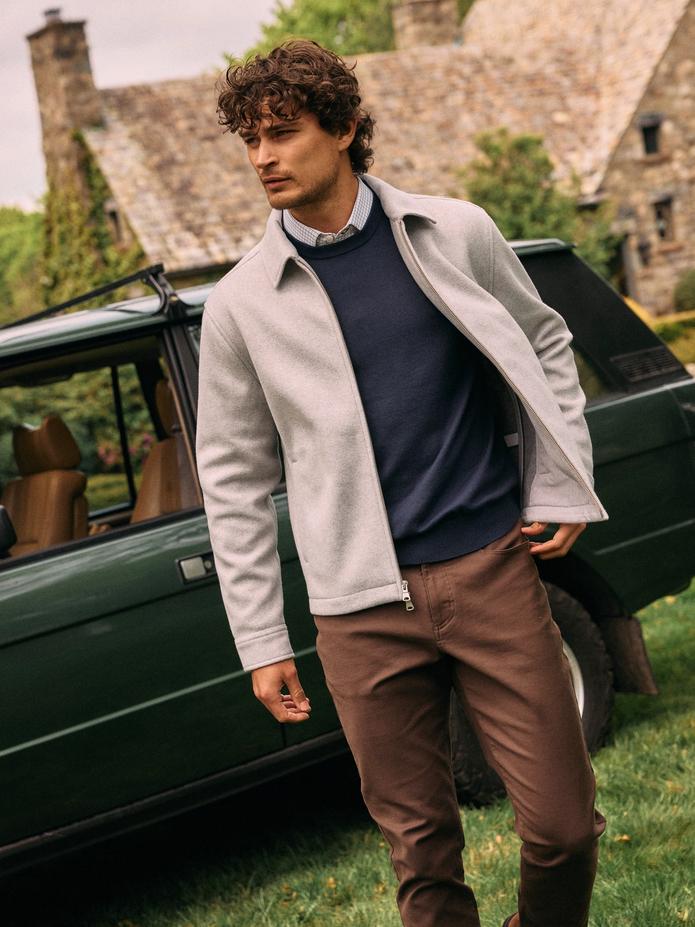 Man in a light gray jacket over a navy sweater and brown pants walking past a vintage green Range Rover