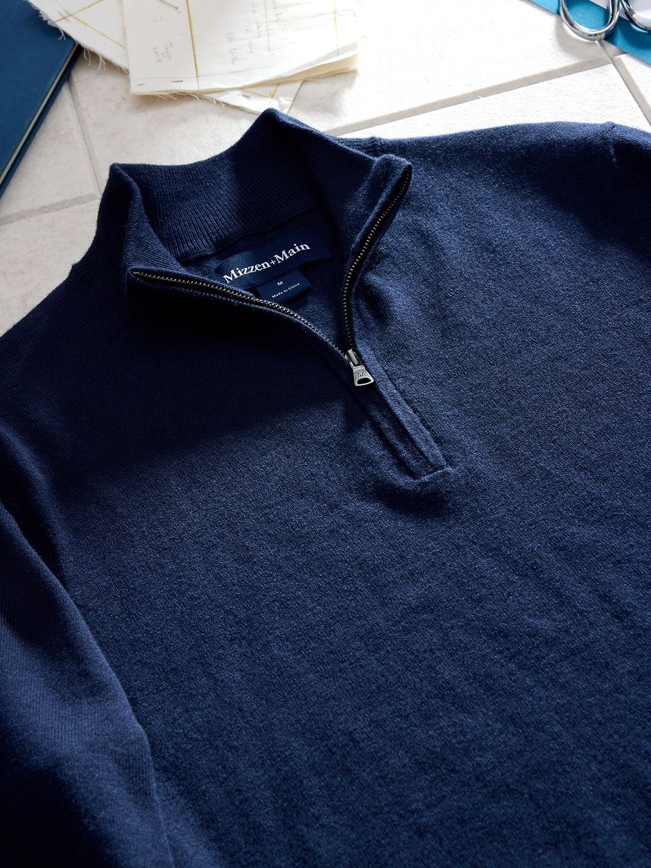 A close-up flat-lay shot of the collar and zipper of a navy blue quarter-zip sweater showing the Mizzen+Main neck tag.