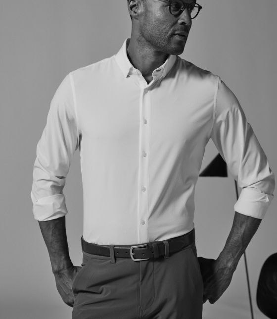 Black-and-white photo of a man in the first white performance fabric dress shirt, sleeves rolled and hands in his pockets.