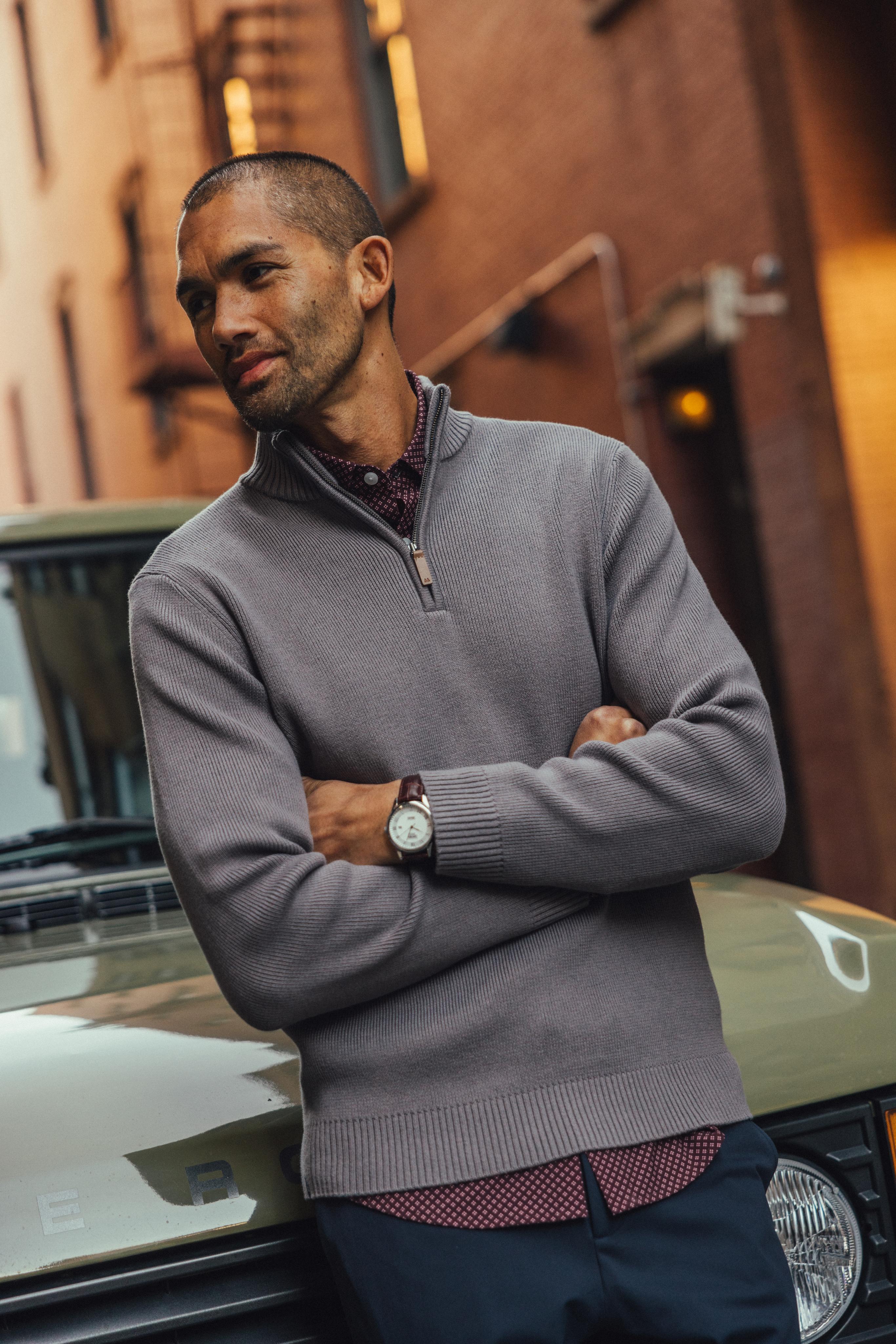 Man in a gray Hillcrest quarter zip sweater leaning against a vintage truck on a city street