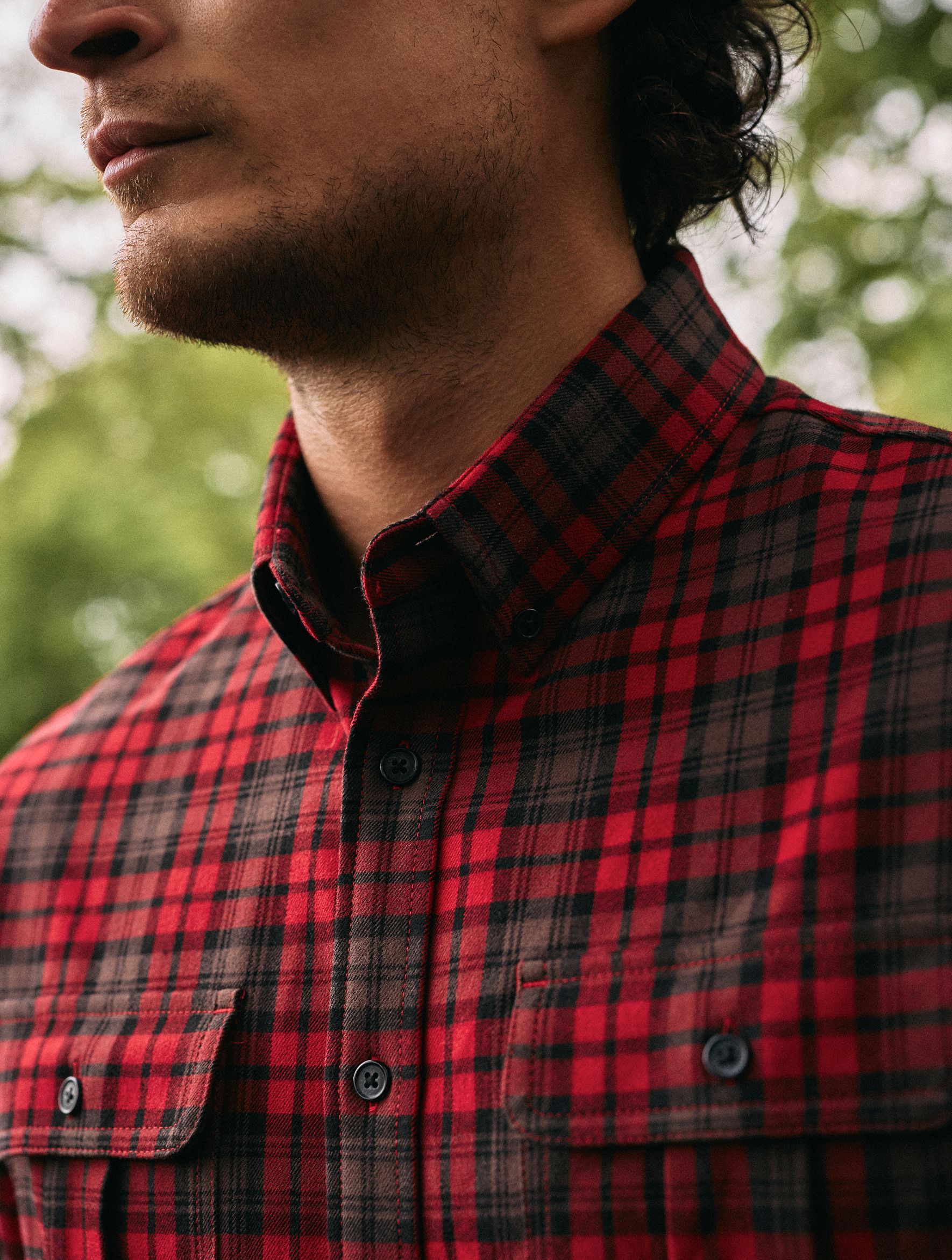 A close-up shot of a man wearing a red and black plaid button-down shirt with chest pockets.