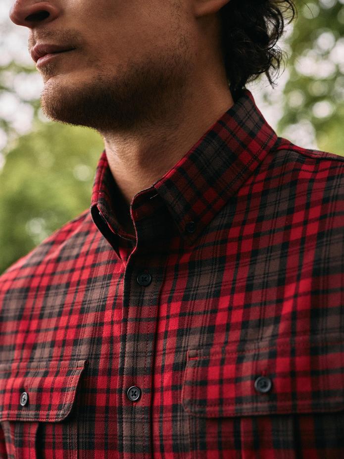 A close-up shot of a man wearing a red and black plaid button-down shirt with chest pockets.