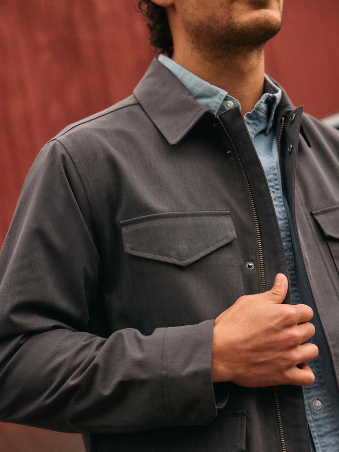 A close-up shot of a man wearing a dark charcoal button-up jacket layered over a light blue shirt.