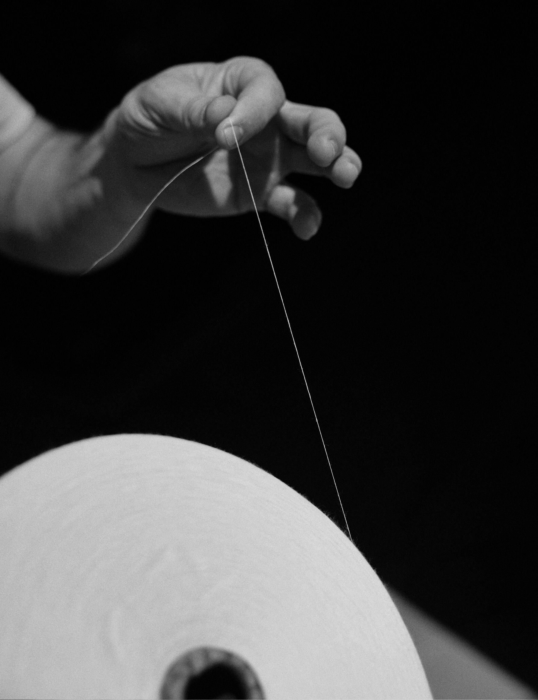 Black-and-white close-up of a worker pulling a single strand of thread from a large paper spool.