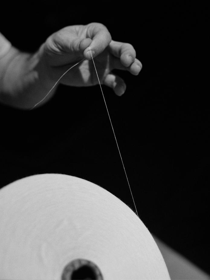 Black-and-white close-up of a worker pulling a single strand of thread from a large paper spool.