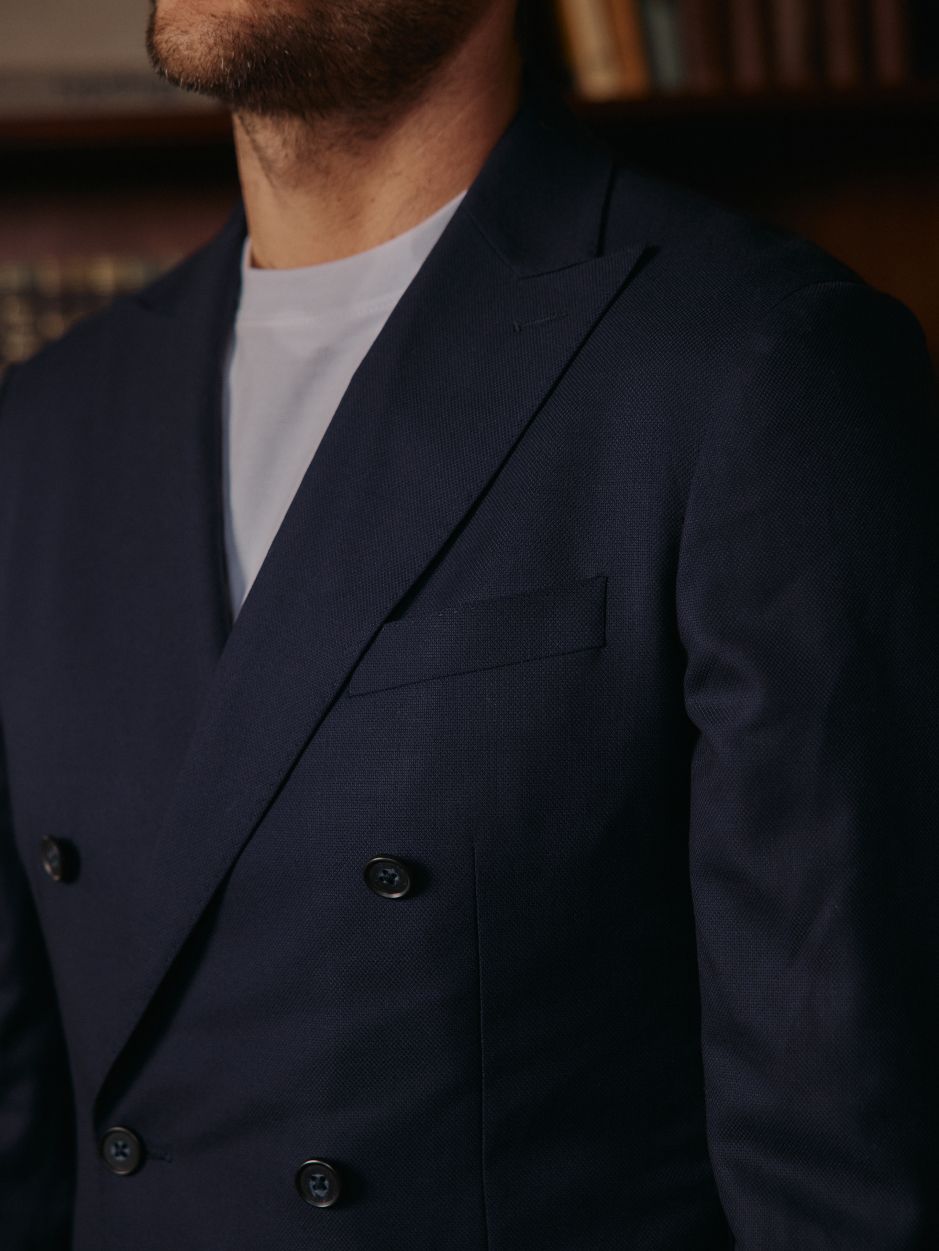 A close-up shot of a man wearing a double-breasted navy blue blazer layered over a simple white t-shirt.