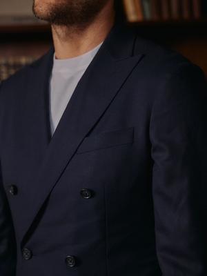 A close-up shot of a man wearing a double-breasted navy blue blazer layered over a simple white t-shirt.