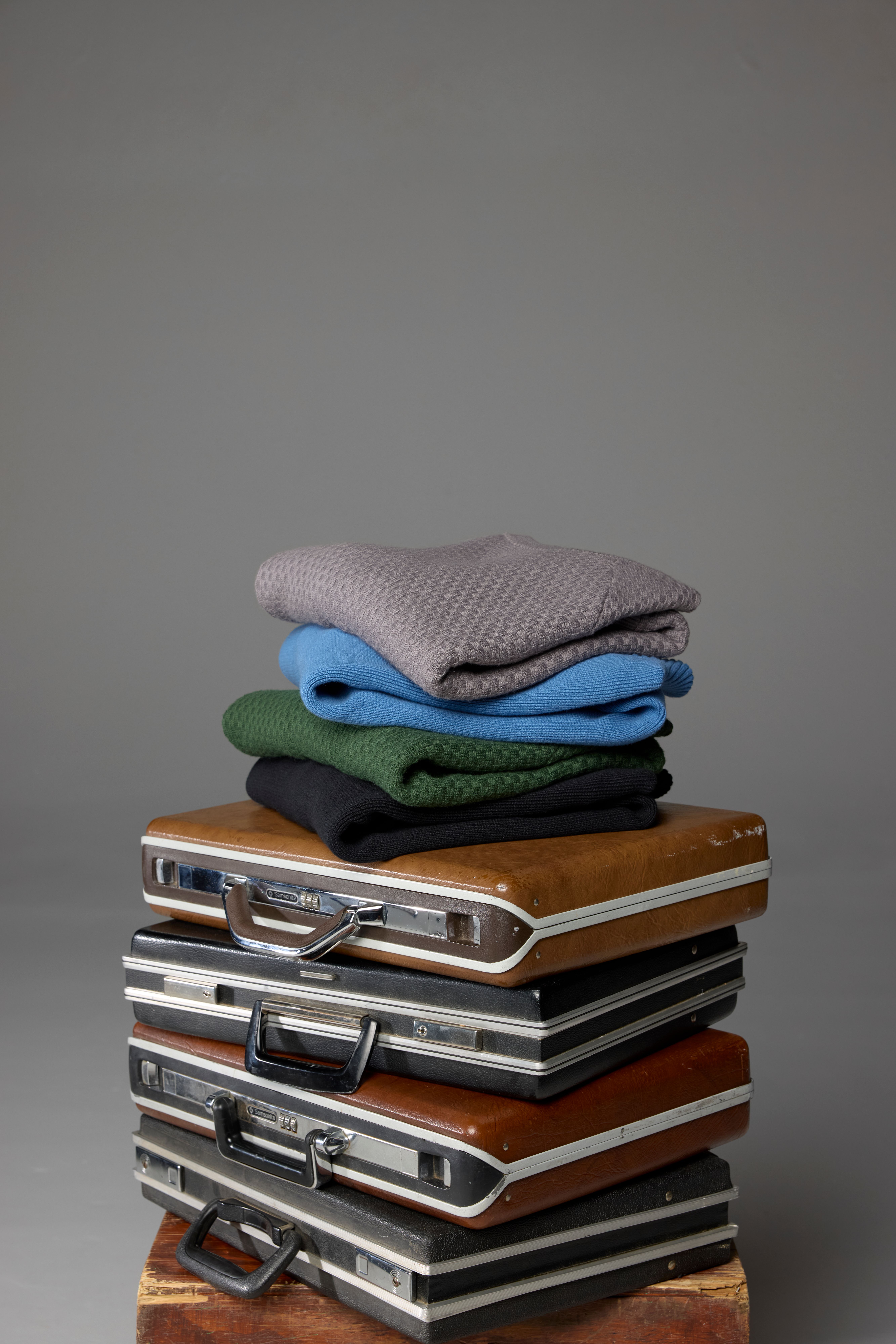 Folded Hillcrest sweaters stacked on a pile of vintage briefcases