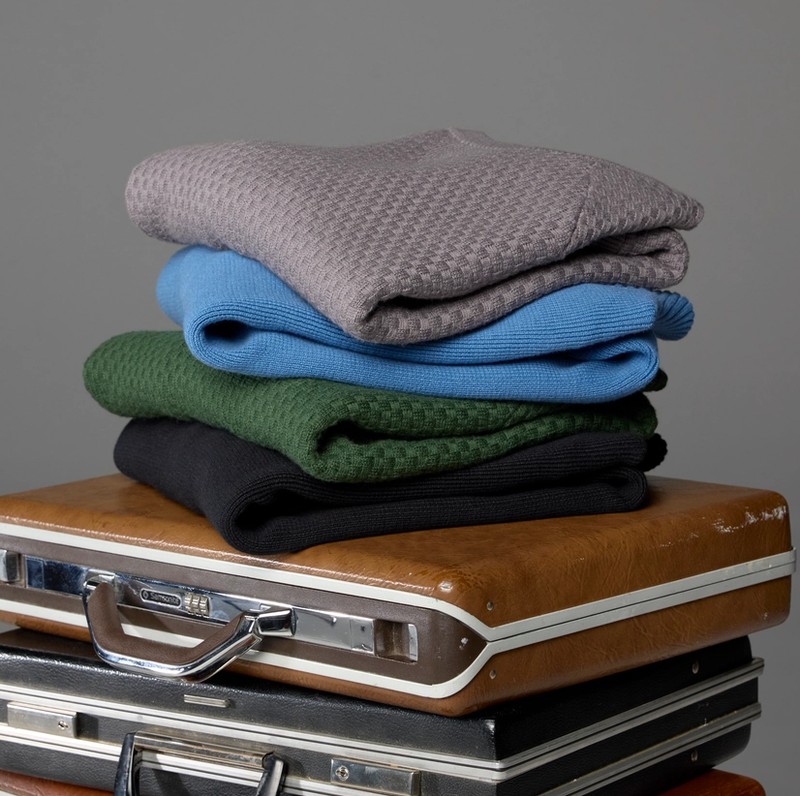 Folded Hillcrest sweaters stacked on a pile of vintage briefcases