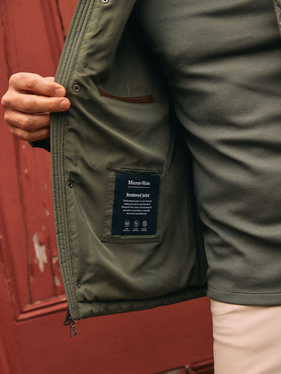 A close-up interior view of an olive green jacket, showing the inner lining and the "Mizzen+Main Brentwood Jacket" label.