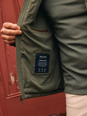 A close-up interior view of an olive green jacket, showing the inner lining and the "Mizzen+Main Brentwood Jacket" label.