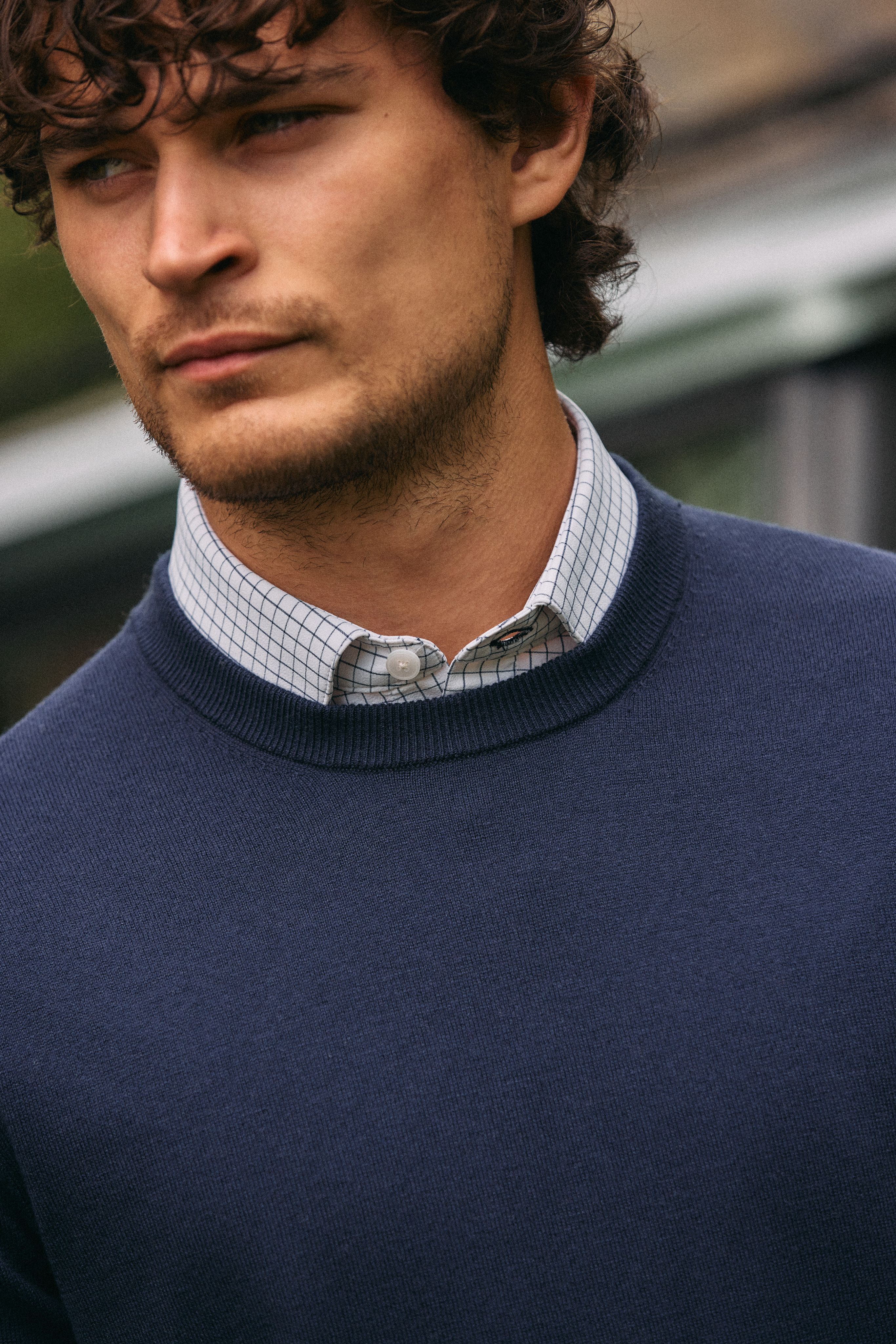 Close-up of a navy crewneck sweater layered over a checked collared shirt