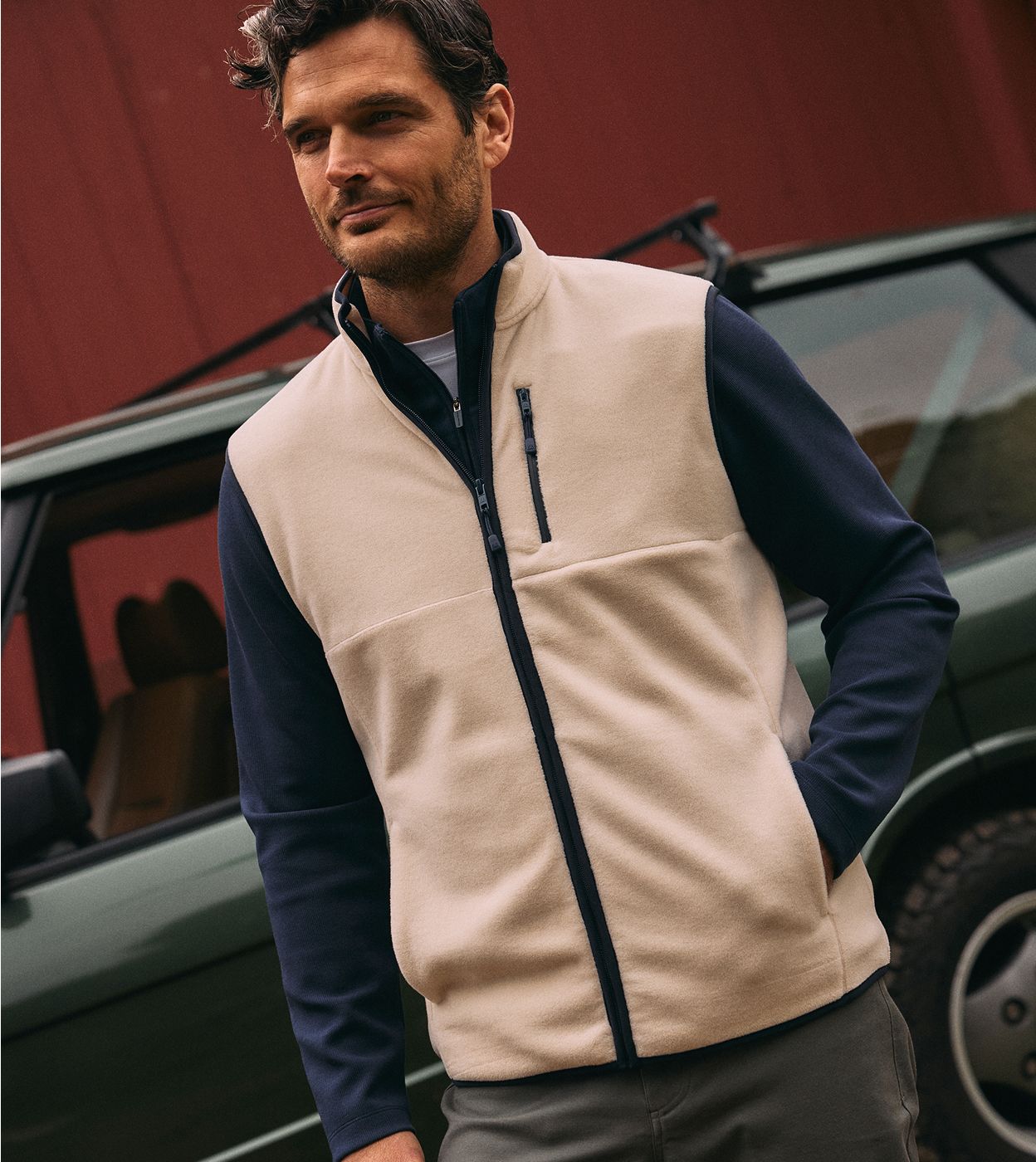 Man in an oat Crosby Fleece Vest over a navy long-sleeve shirt, standing beside a green car.
