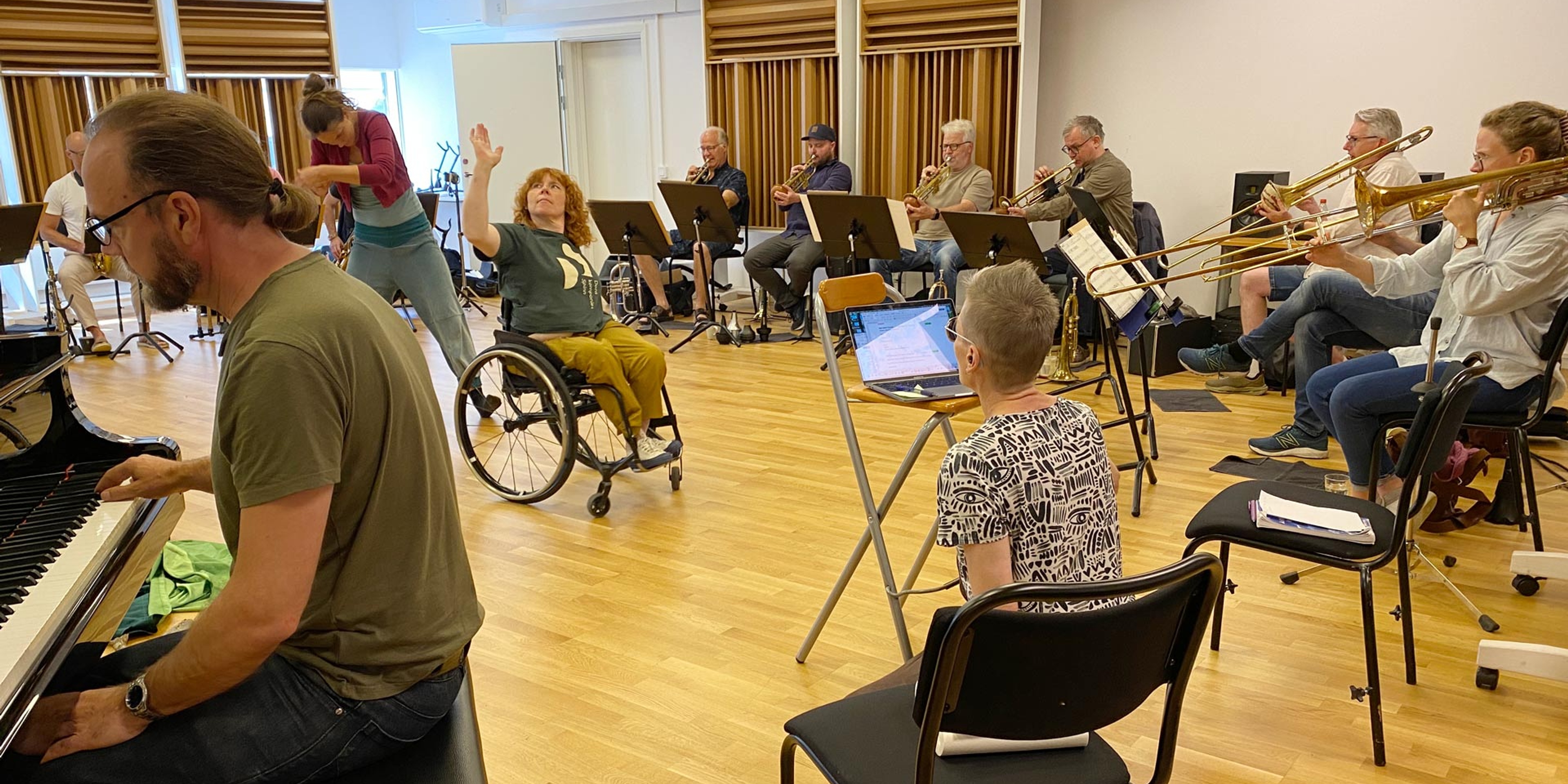 Musikerna i Bohuslän Big Band spelar i en repsal tillsammans med dansare, varav en sitter i rullstol.