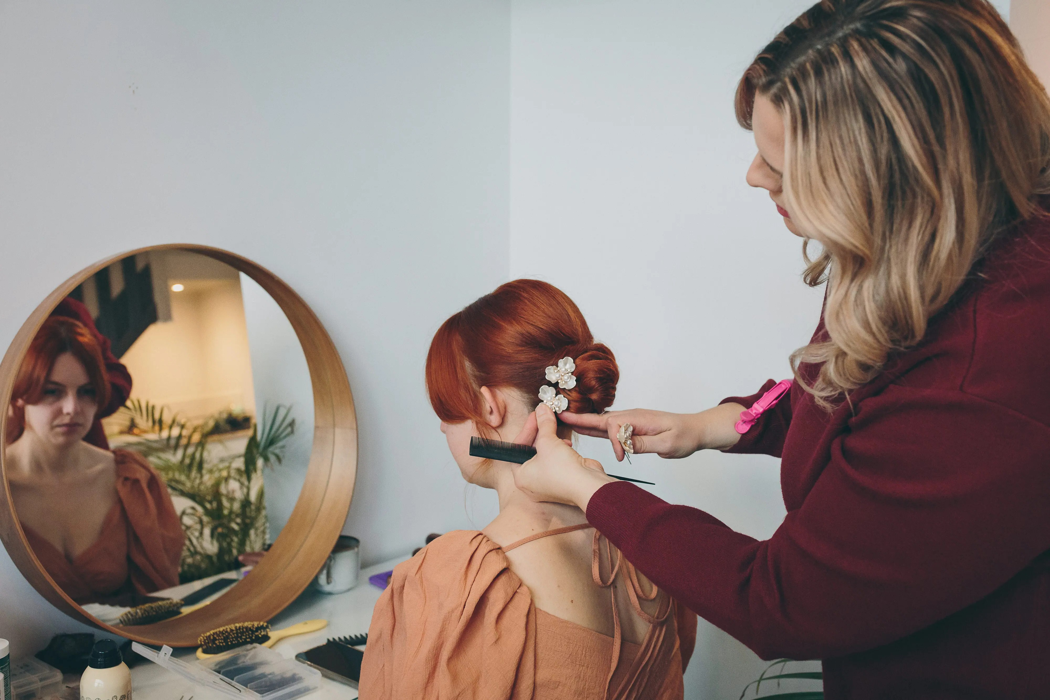 A bride with copper red hair having her hair done with lady in burgundy dress