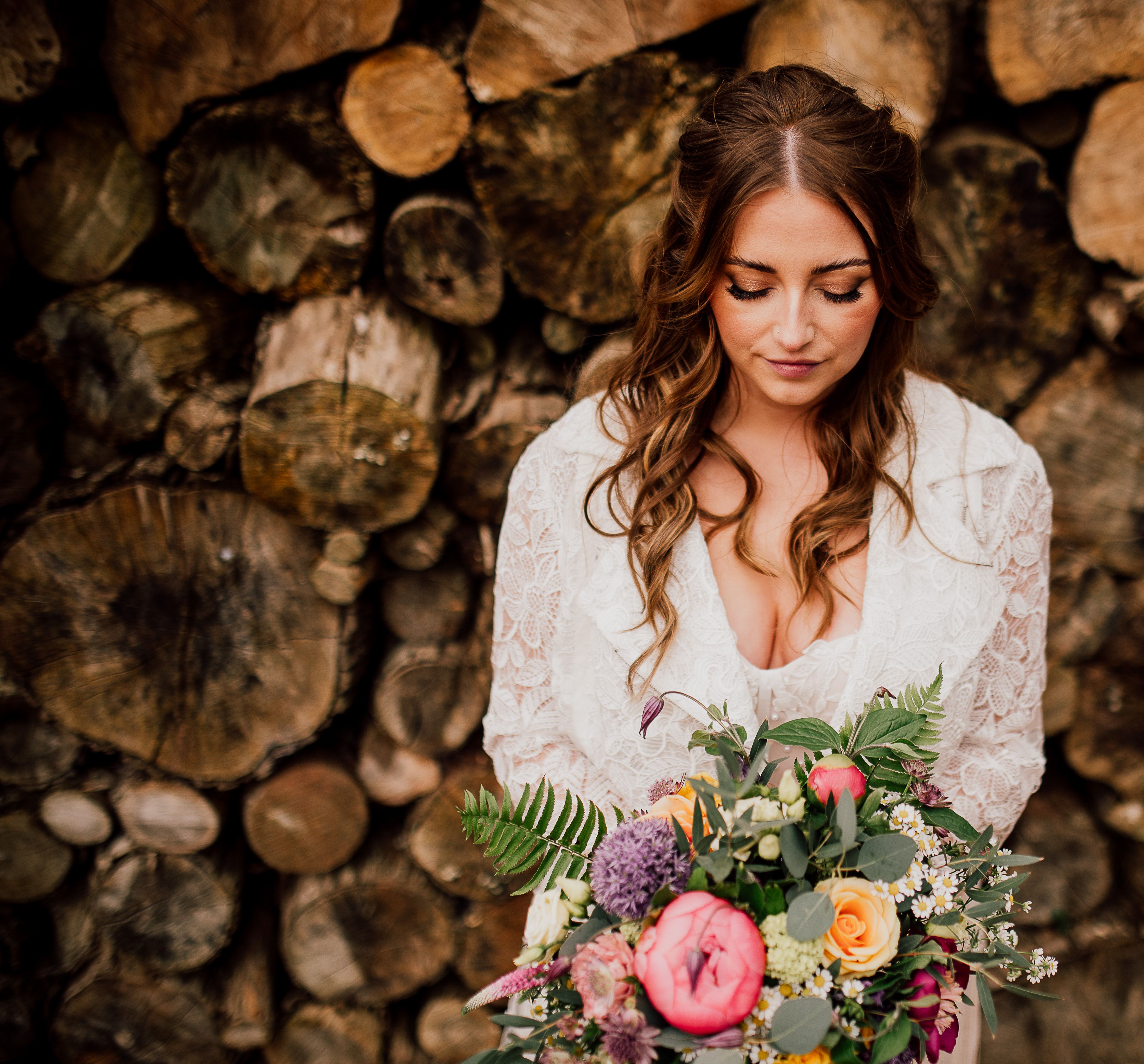 A bride down surrounded by logs with an array of vibrant, colourful flowers.