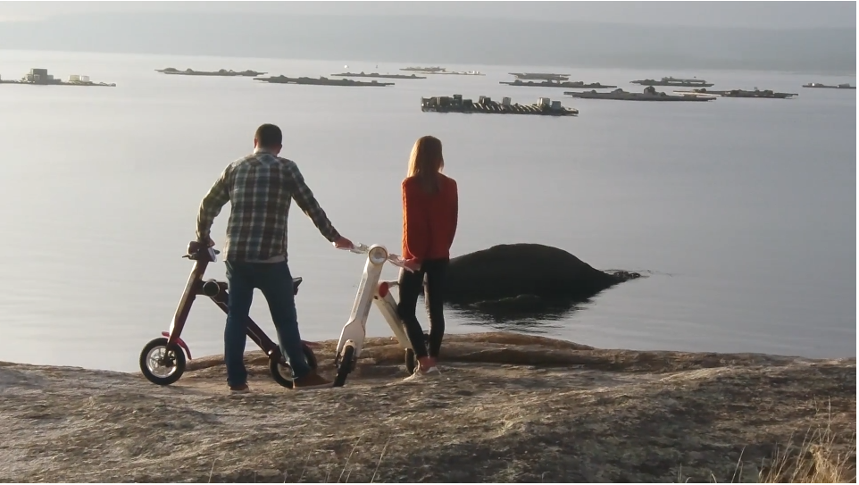 Dos personas junto a vehículos eléctricos Shadow Mobility frente al mar, en una escena del spot publicitario de la marca.