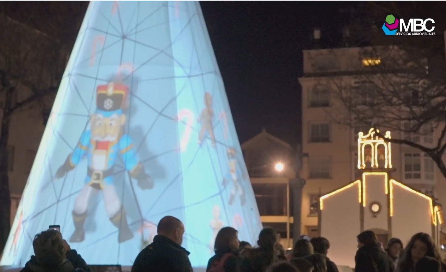 Proyección de videomapping navideño sobre un gran árbol de Navidad en As Pontes, con la animación de un cascanueces y público contemplando el espectáculo.