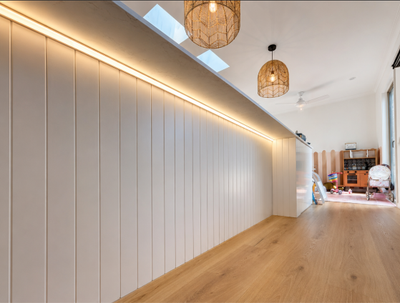 Warm LED strip lighting installed beneath a kitchen island bench, paired with woven pendant lights and timber flooring in a renovated Tewantin home.
