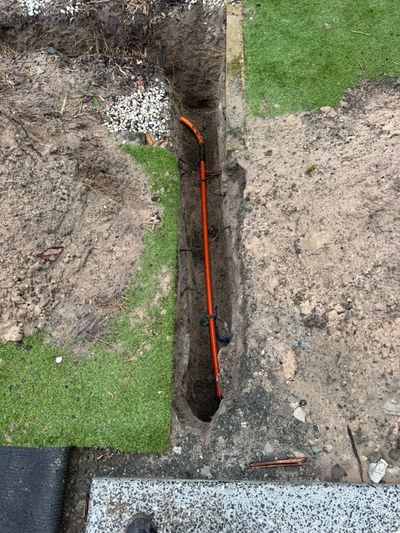 Orange conduit in a narrow trench cut through turf at Mossman Court