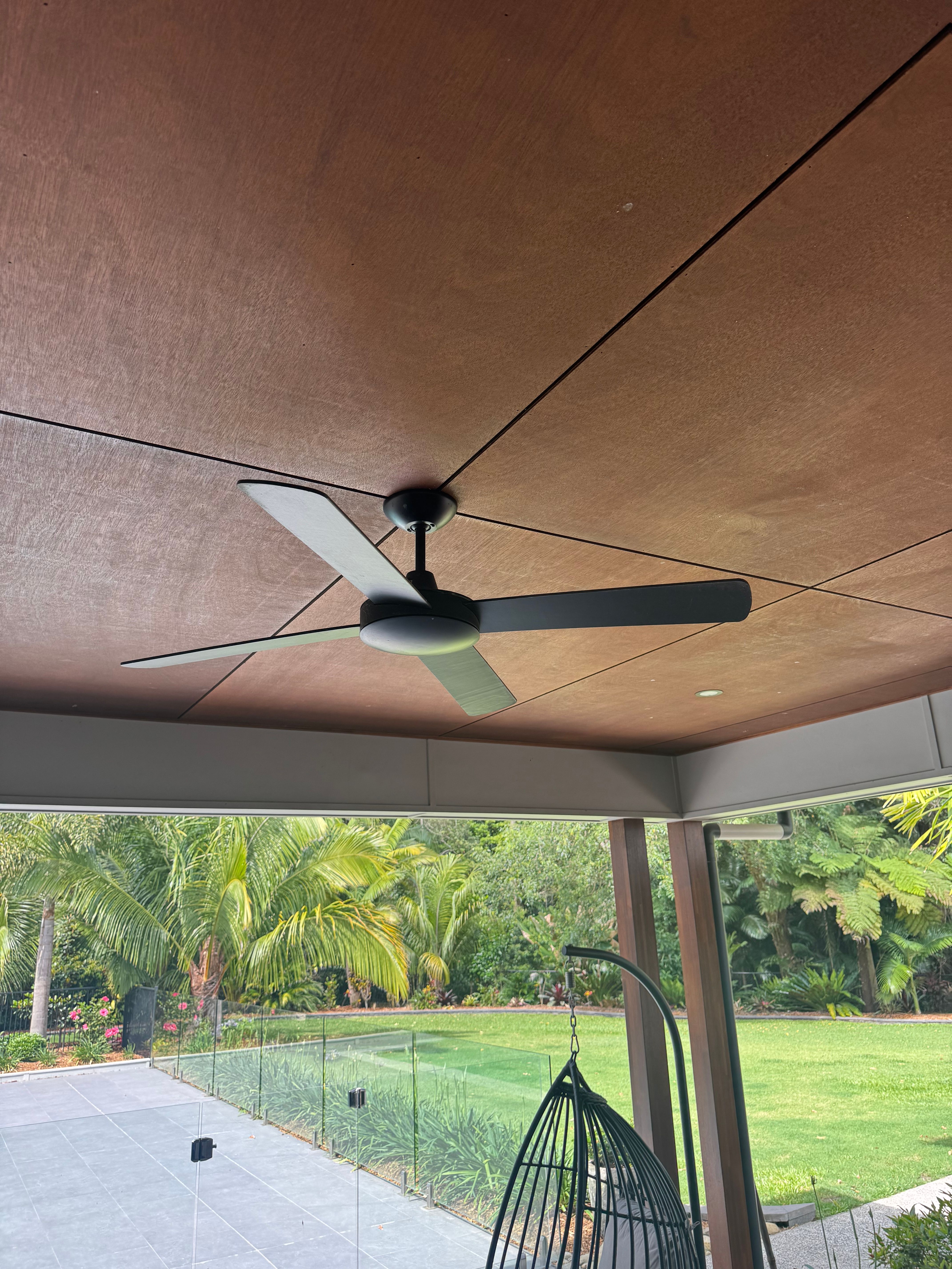 Black ceiling fan mounted beneath a timber-lined alfresco ceiling overlooking the garden